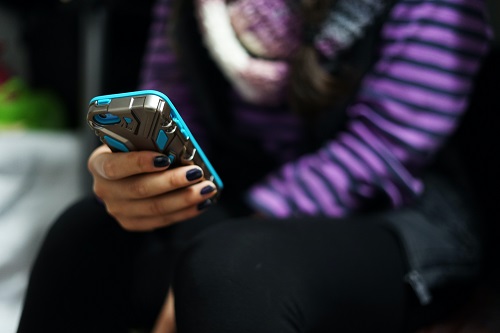 Girl in purple and black stripy top holding a blue smartphone